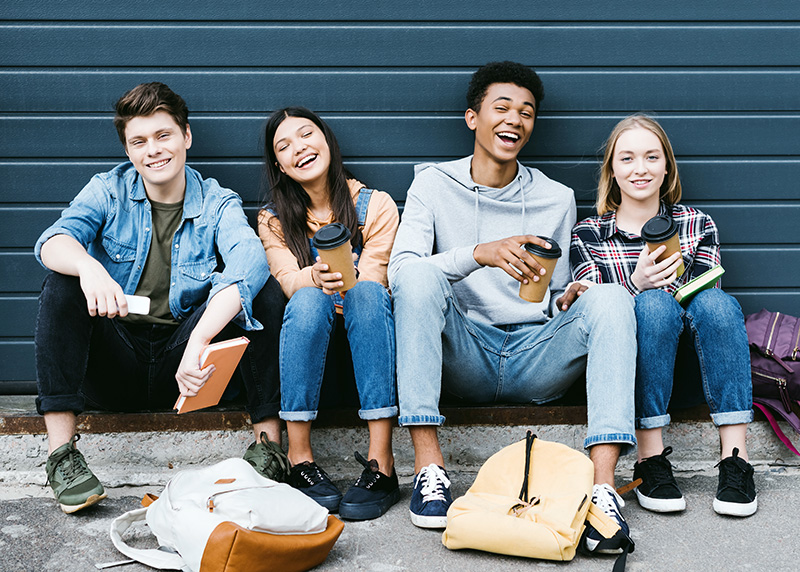 advocating-for-youth Group of diverse teens sitting outside, smiling and holding drinks, representing youth engagement, peer support, and positive community programs.