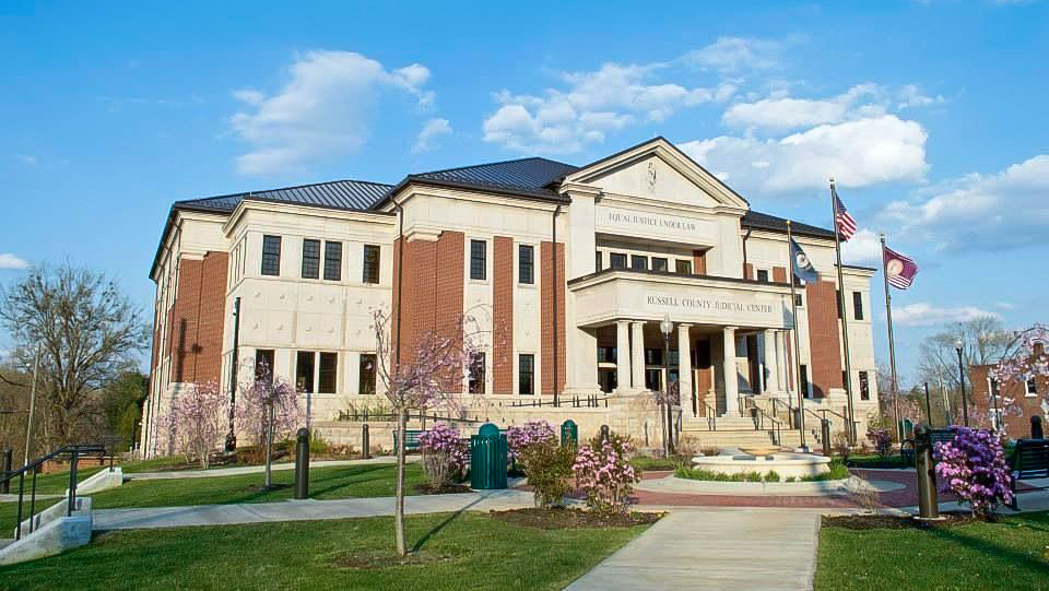russell-county-judicial-center Exterior of the Russell County Judicial Center in Kentucky, with flags flying and spring landscaping in bloom under a blue sky.